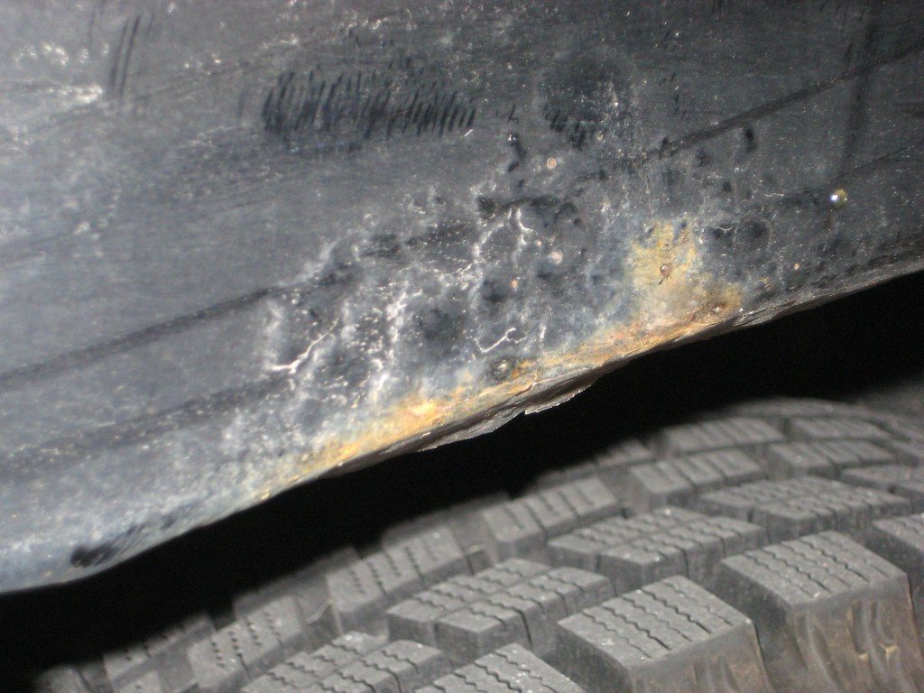 Borde interior del paso de rueda trasero de un Mazda MX-5, con el óxido empezando a salir bajo la pintura, justo encima del neumático.